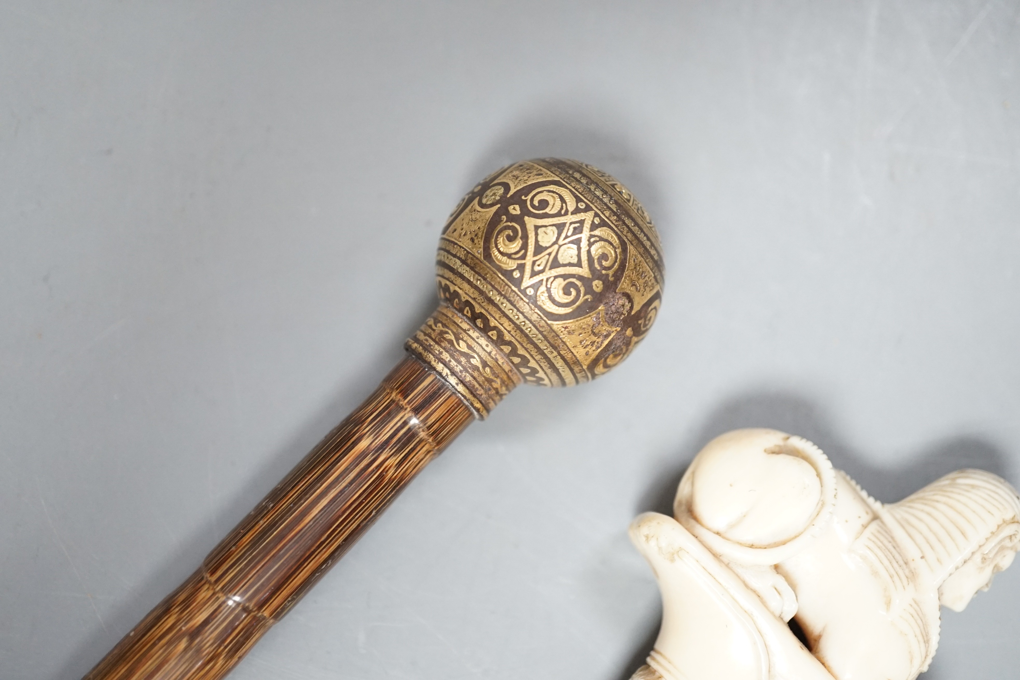 An early 20th century ivory ‘sphinx’ parasol handle, 84cm, together with another gold and iron damascened parasol handle, 62cm